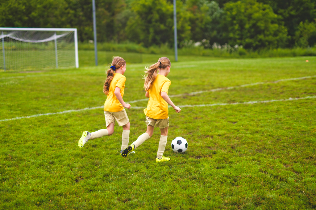 Children playing football on a green field.